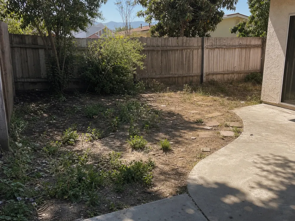 Before view of a small Pomona backyard corner with bare soil, weeds, and a worn patio edge